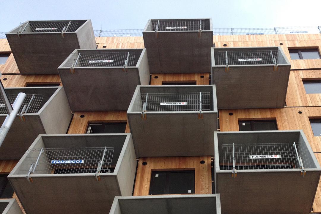 Blick von unten auf die Holzfassade mit den Betonbalkonen und provisorischen Geländern