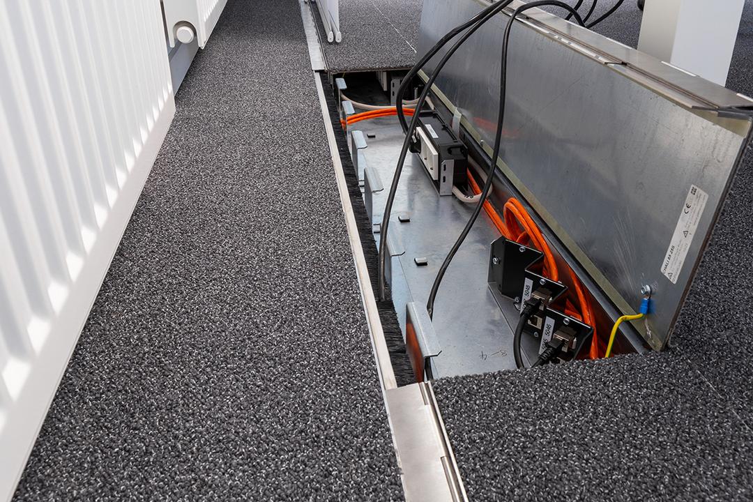 Geöffneter Bodenkanal im Teppichboden mit Strom- und Datenanschlüssen sowie verlegten Kabeln für Büroarbeitsplätze.