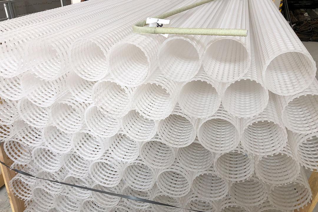 Gestapelte weiße Kunststoffrohre mit Gitterstruktur, darauf ein einzelner heller Bewehrungsstab abgelegt