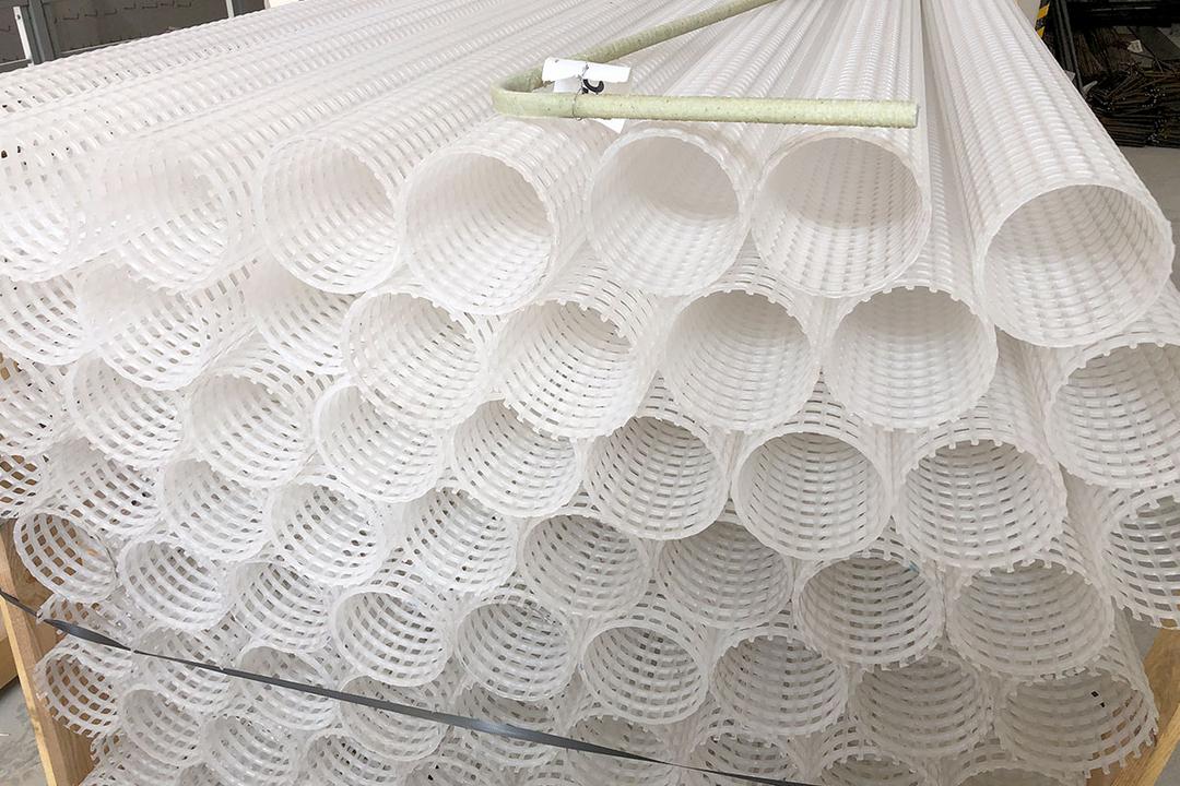 Gestapelte weiße Kunststoffrohre mit Gitterstruktur, darauf ein einzelner heller Bewehrungsstab abgelegt