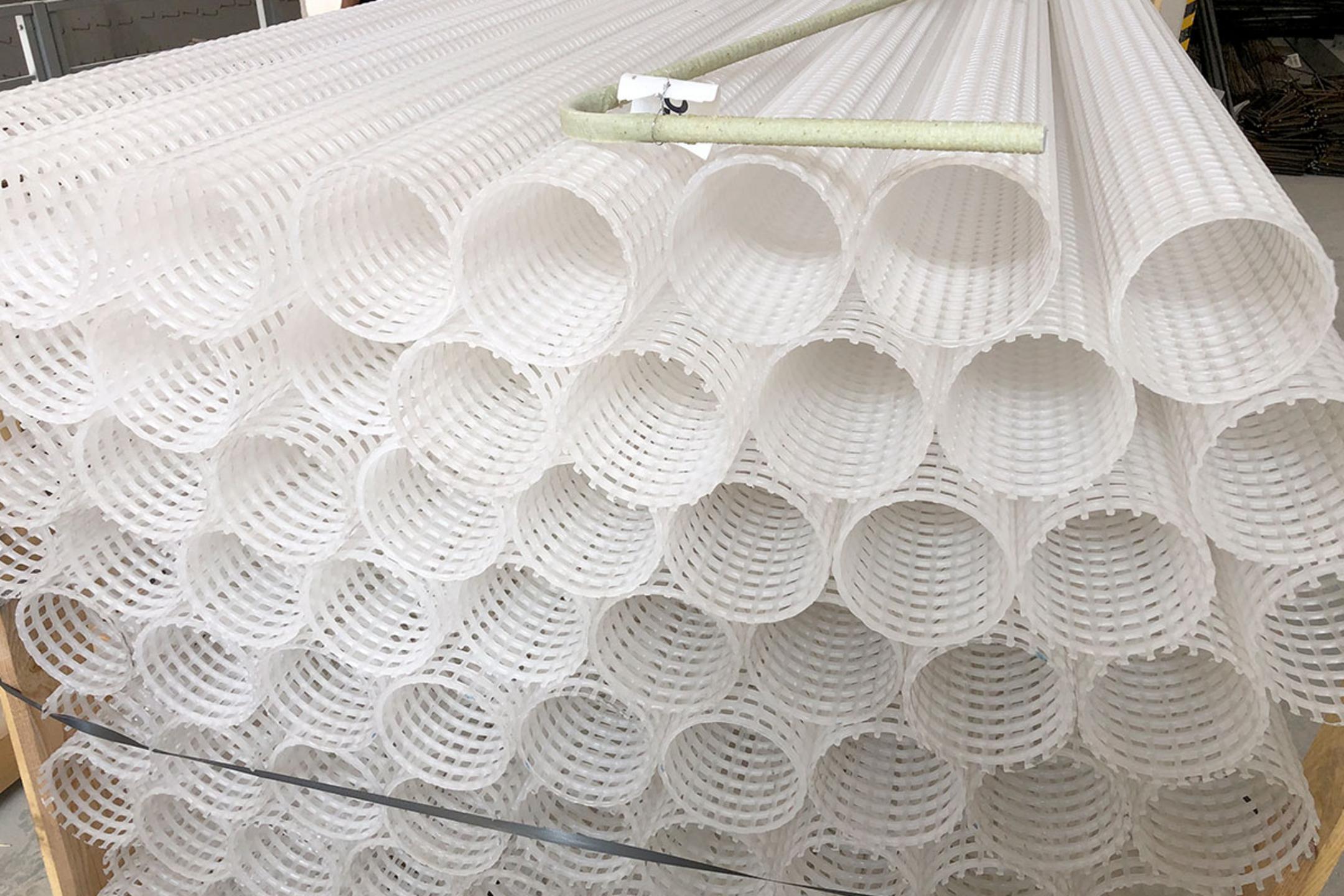 Gestapelte weiße Kunststoffrohre mit Gitterstruktur, darauf ein einzelner heller Bewehrungsstab abgelegt