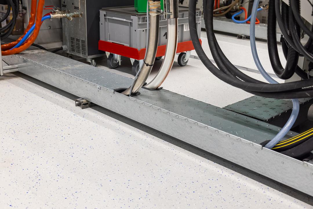 Detailansicht begehbarer Bodenkanal mit Produktionsmaschinen im Hintergrund.