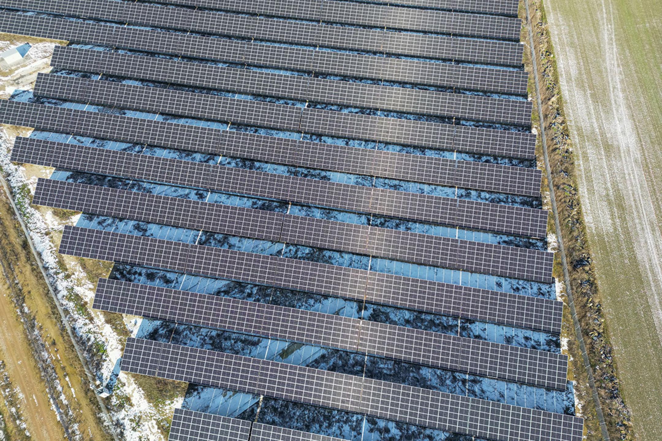 Draufsicht auf einen Solarpark, umgeben von Feldern, teilweise von Schnee bedeckt