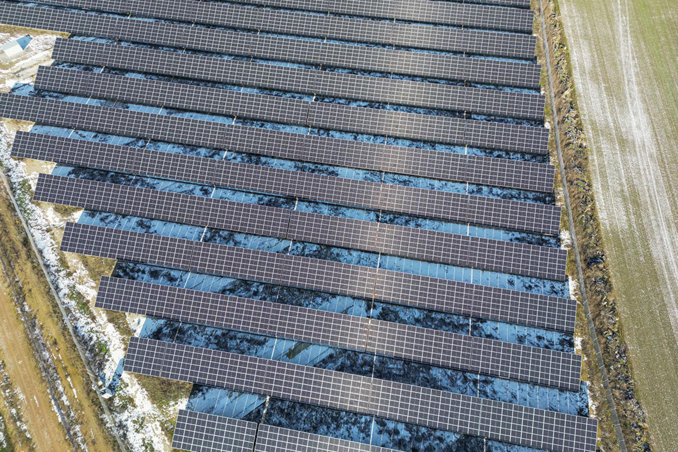 Draufsicht auf einen Solarpark, umgeben von Feldern, teilweise von Schnee bedeckt