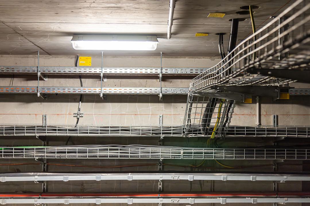 Gitterbahnen und Kabeltrassen montiert an der Decke und der Wand eines Raumes, beleuchtet durch eine Deckenleuchte