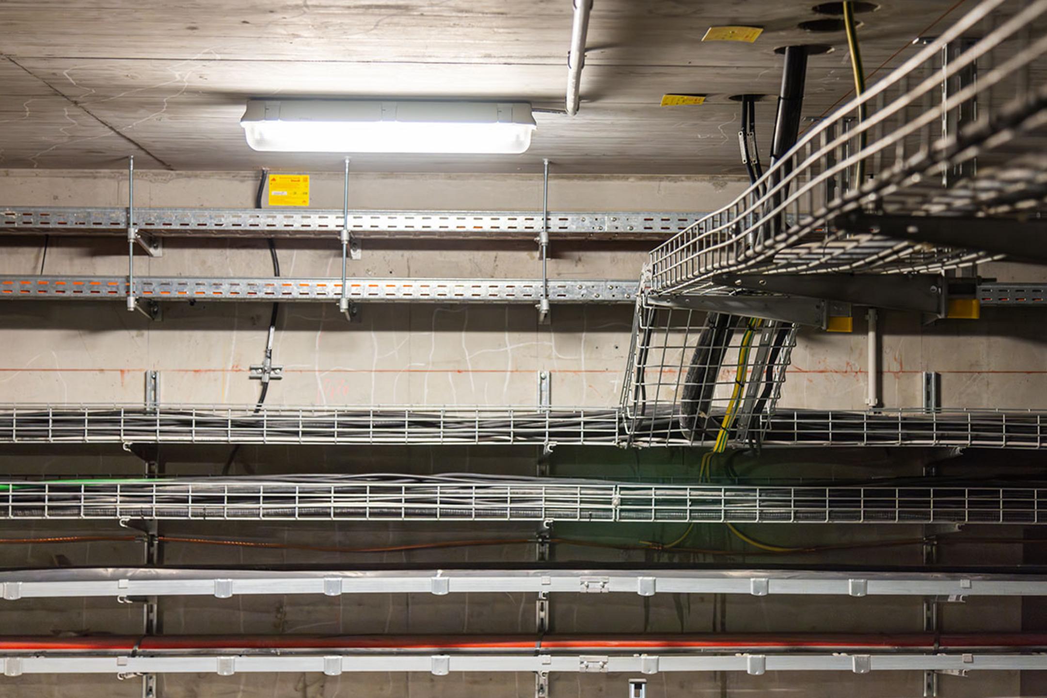 Gitterbahnen und Kabeltrassen montiert an der Decke und der Wand eines Raumes, beleuchtet durch eine Deckenleuchte
