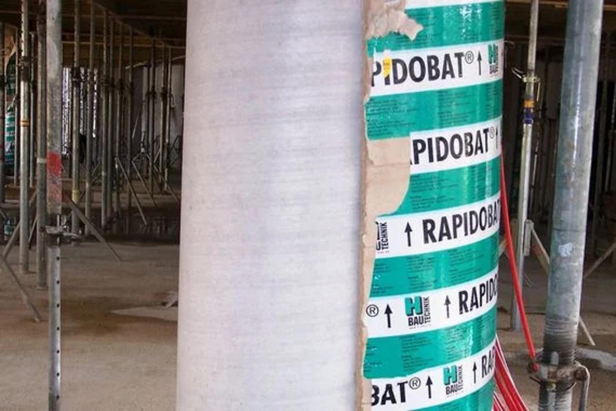 Baustelle mit großem Betonpfeiler, teilweise ist noch der Schalungskörper mit Aufschrift 'Rapidobat' zu erkennen, umgeben von Gerüsten und Trägern