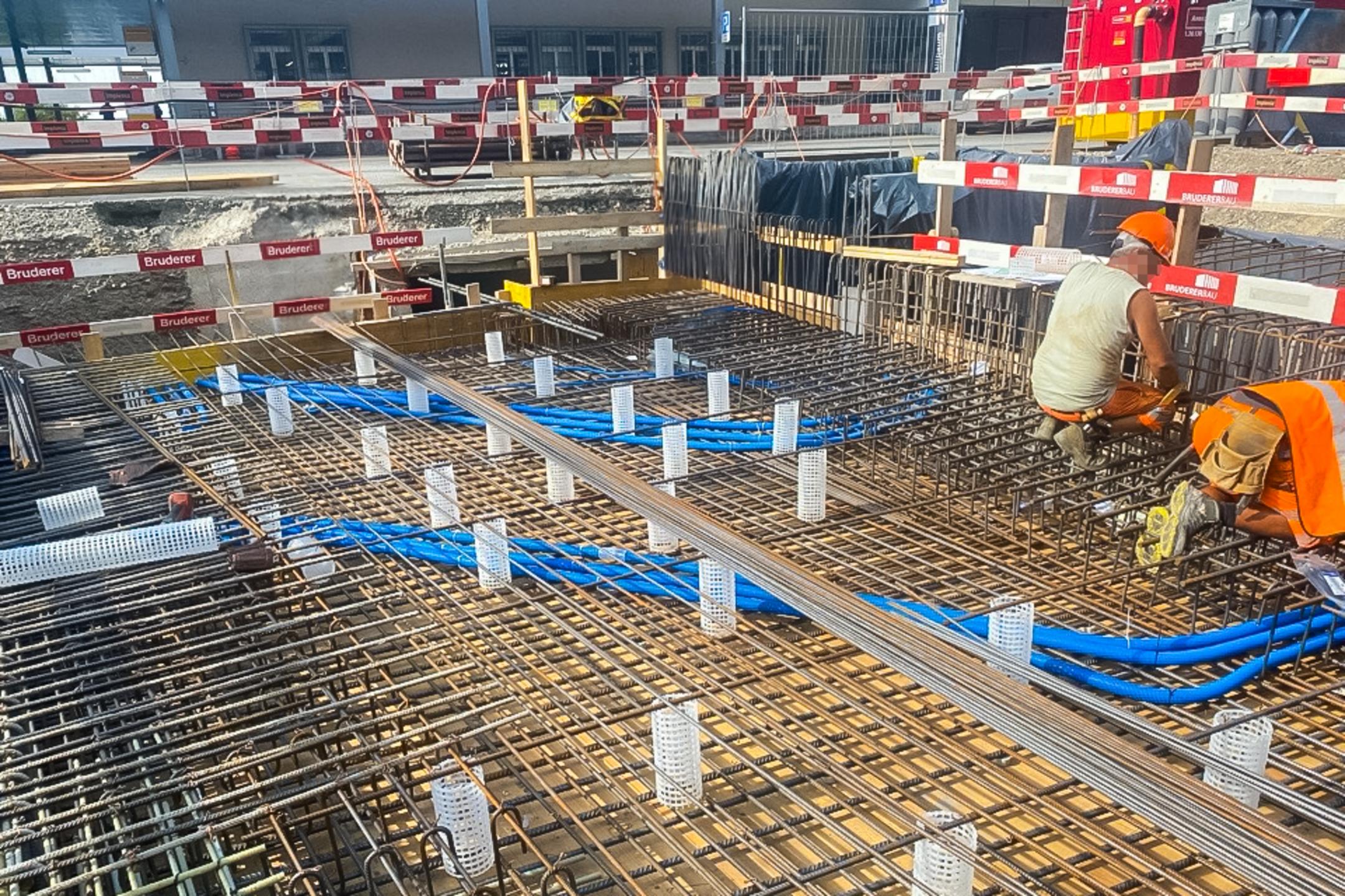 Arbeiter installieren Bewehrung und Leitungen in einer Bodenplatte auf einer abgesicherten Baustelle