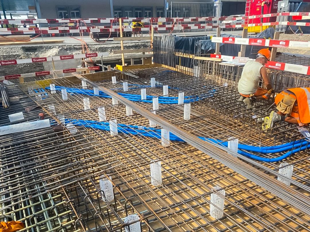 Arbeiter installieren Bewehrung und Leitungen in einer Bodenplatte auf einer abgesicherten Baustelle