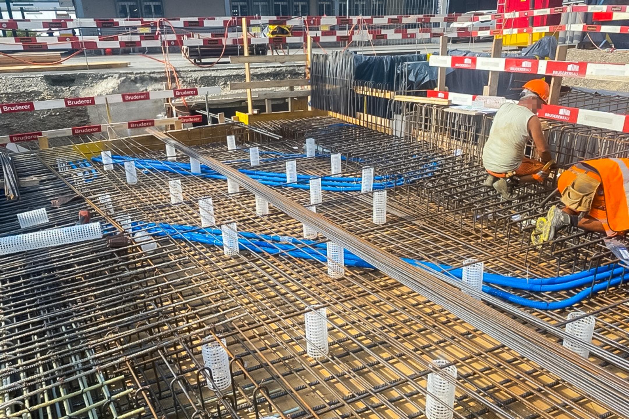 Arbeiter installieren Bewehrung und Leitungen in einer Bodenplatte auf einer abgesicherten Baustelle