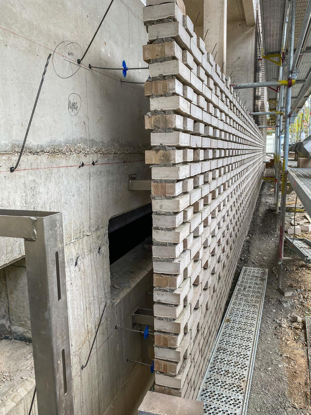 Baustelle mit halbfertiger Mauer aus weißen Ziegeln und Gerüst im Außenbereich