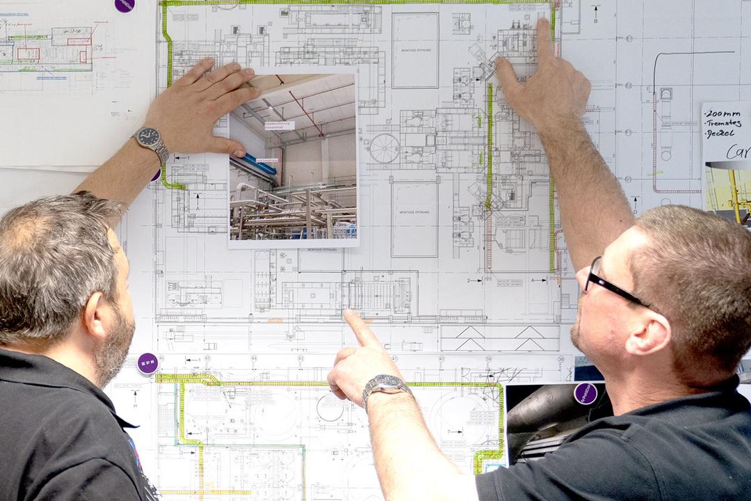 Zwei Männer stehen vor einem großen Plan zur Technischen Gebäudeausrüstung eines Gebäudes
