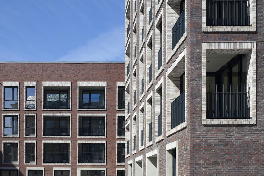 Moderner Wohnkomplex mit Backsteinfassade, großen Fenstern und Balkonen vor blauem Himmel
