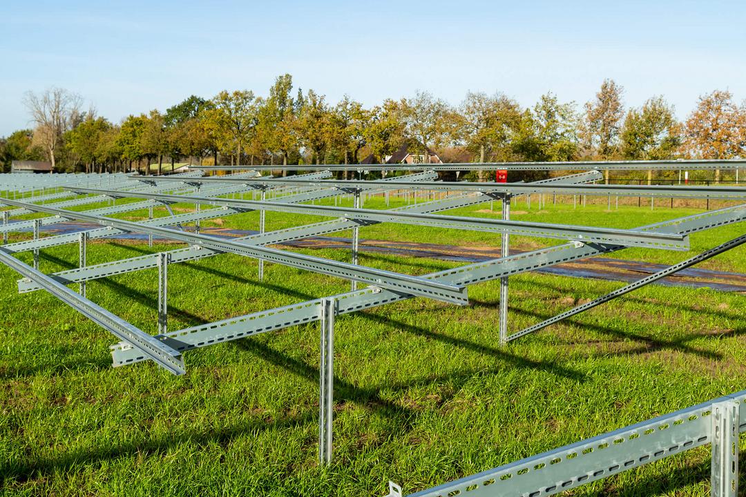 Montierte Stahlunterkonstruktion einer PV-Freiflächenanlage auf grüner Wiese bei Sonnenschein, noch ohne Solarmodule.