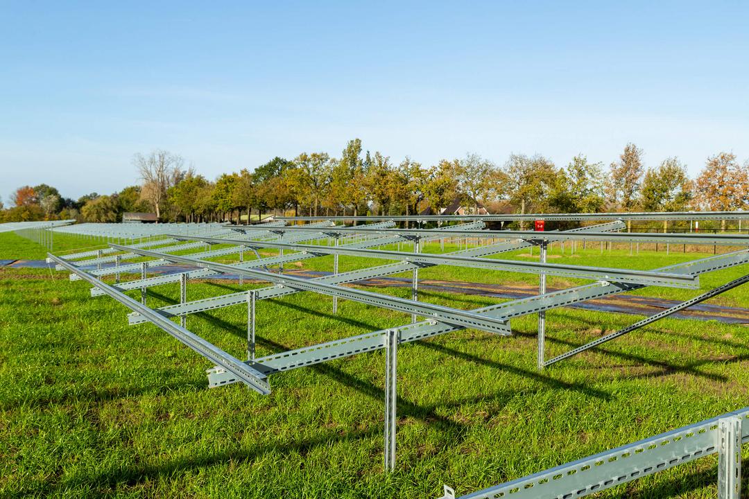 Montierte Stahlunterkonstruktion einer PV-Freiflächenanlage auf grüner Wiese bei Sonnenschein, noch ohne Solarmodule.