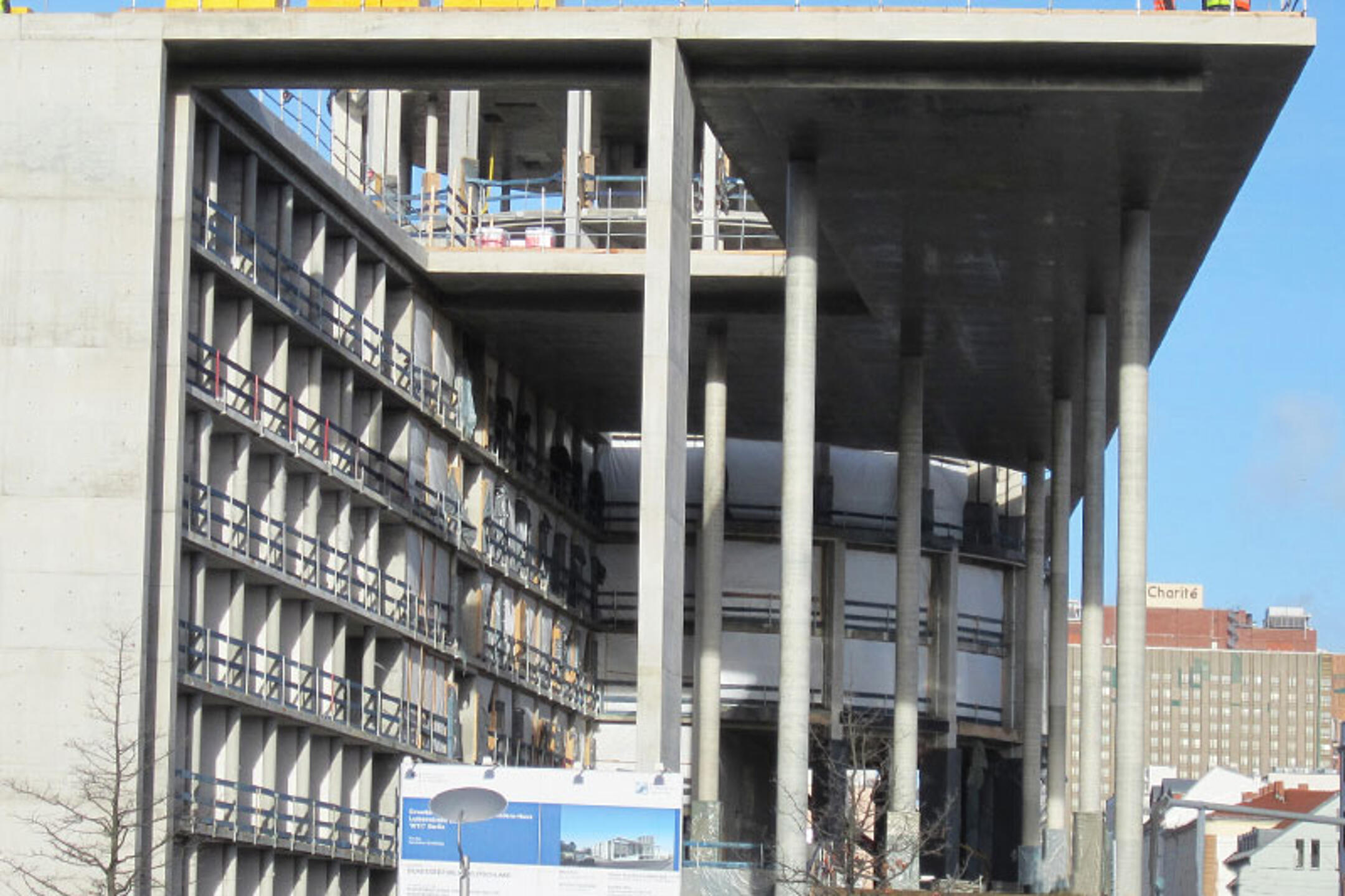 Baustelle eines mehrstöckigen Gebäude im Rohbau mit Betonpfeilern und Gerüsten, im Hintergrund ist das Gebäude der Charité zu sehen