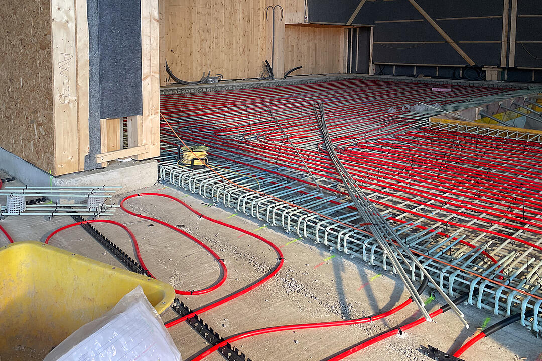 GFK-Bewehrung auf dem Boden verlegt, rote Schläuche auf dem Boden, im Hintergrund holzverkleidete Wände.