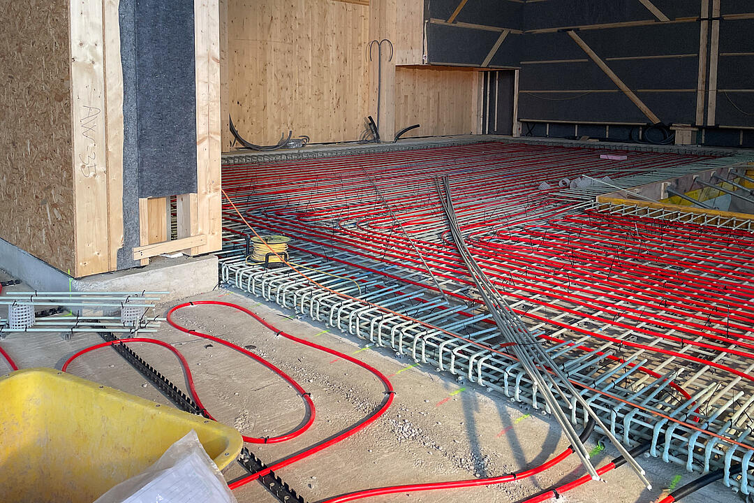 GFK-Bewehrung auf dem Boden verlegt, rote Schläuche auf dem Boden, im Hintergrund holzverkleidete Wände.