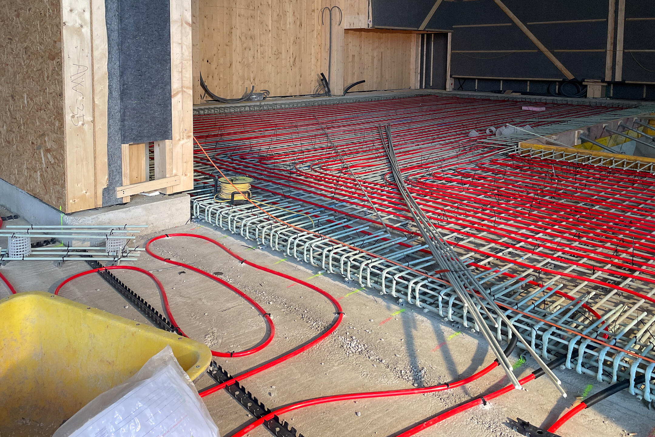 GFK-Bewehrung auf dem Boden verlegt, rote Schläuche auf dem Boden, im Hintergrund holzverkleidete Wände.
