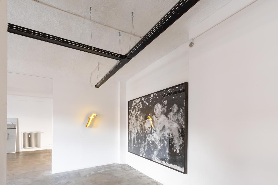 Blick in die Ecke eines Raum mit einem abstrakten Bild und einem Leuchtelement an der Wand hängend. Im oberen Bildausschnitt sieht man eine T-Kreuzung von schwarzen Kabelrinnen.