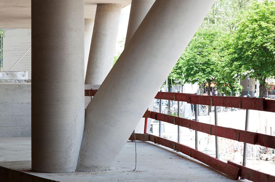 Schräg und senkrecht verlaufende Betonstützen eines Rohbaus unter einer Betondecke mit Blick ins Freie