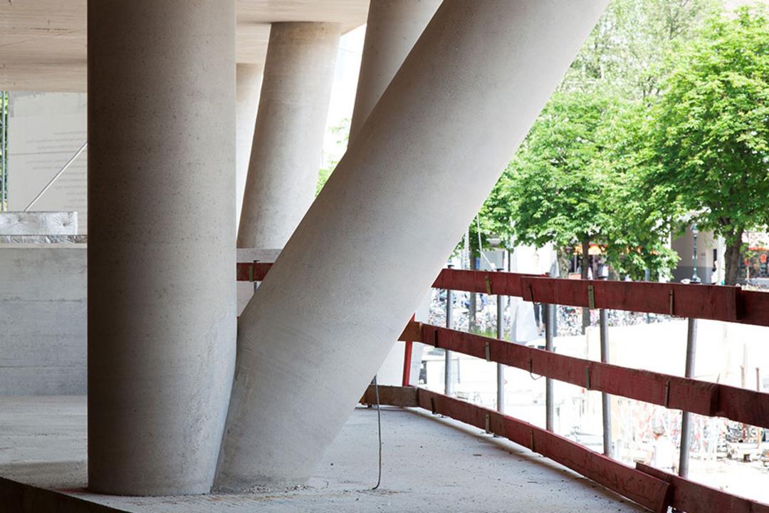 Schräg und senkrecht verlaufende Betonstützen eines Rohbaus unter einer Betondecke mit Blick ins Freie