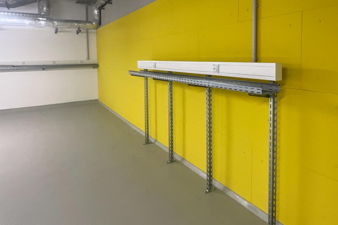 Montage eines Kabeltragsystems an gelber Wand mit vertikalen Tragschienen, waagerechtem Träger und installierter Brüstungskanalleiste.