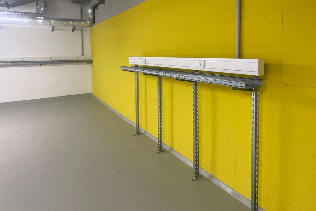 Montage eines Kabeltragsystems an gelber Wand mit vertikalen Tragschienen, waagerechtem Träger und installierter Brüstungskanalleiste.