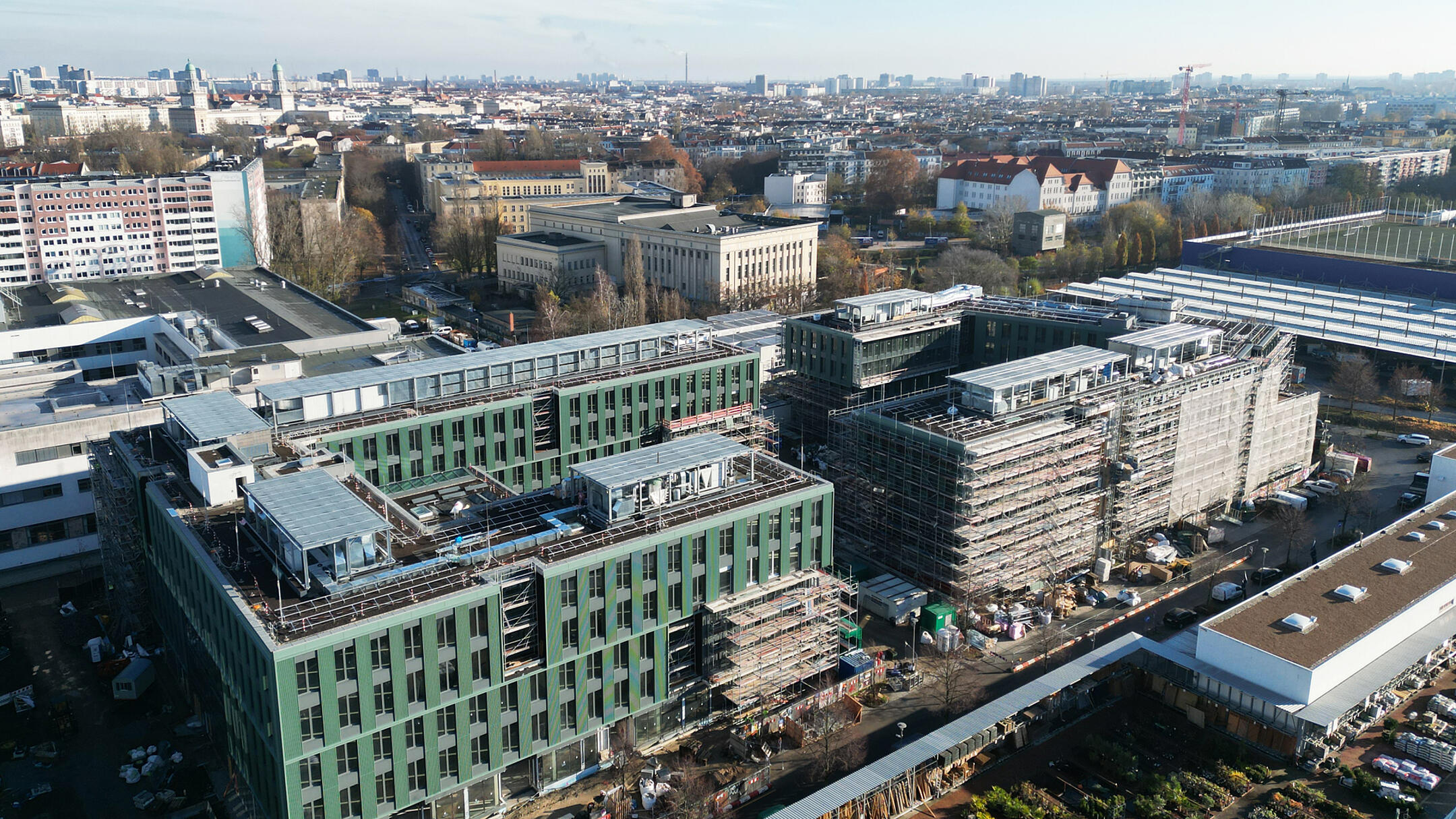 Luftaufnahme eines Gebäudes mit Gerüsten, im Hintergrund Blick auf Stadt und blauer Himmel.