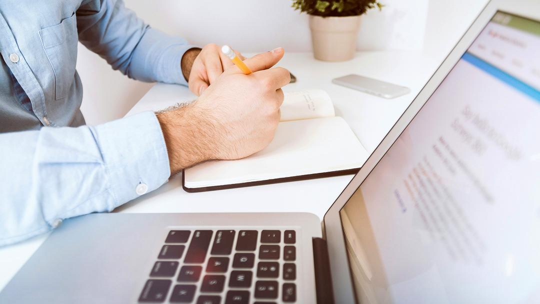 Mann sitzt vor Laptop am Schreibtisch und macht sich Notizen
