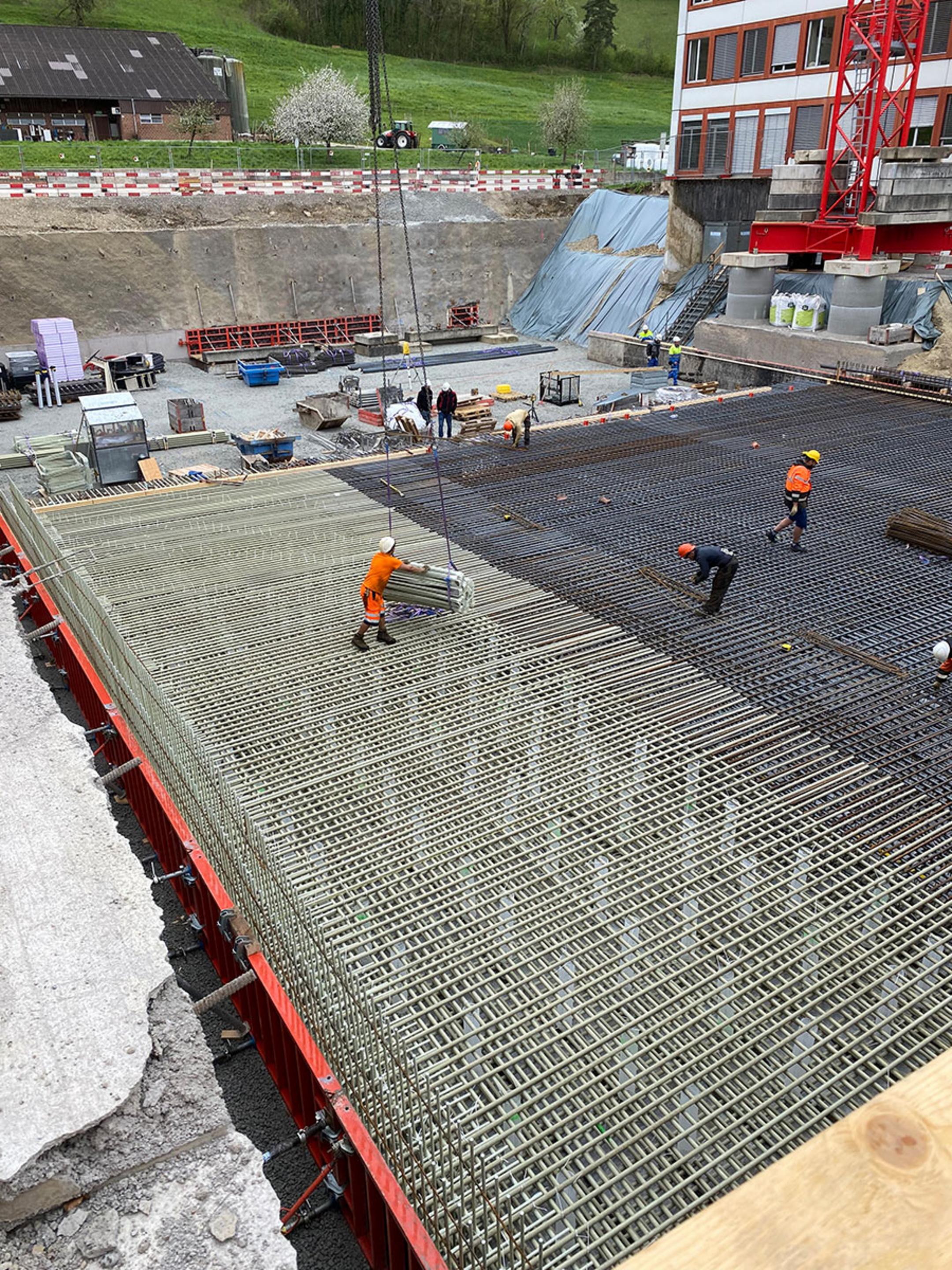 Bauarbeiter verlegen Bewehrungsmatten auf einer Schalung, Kran liefert weiteres Material auf die Baustelle