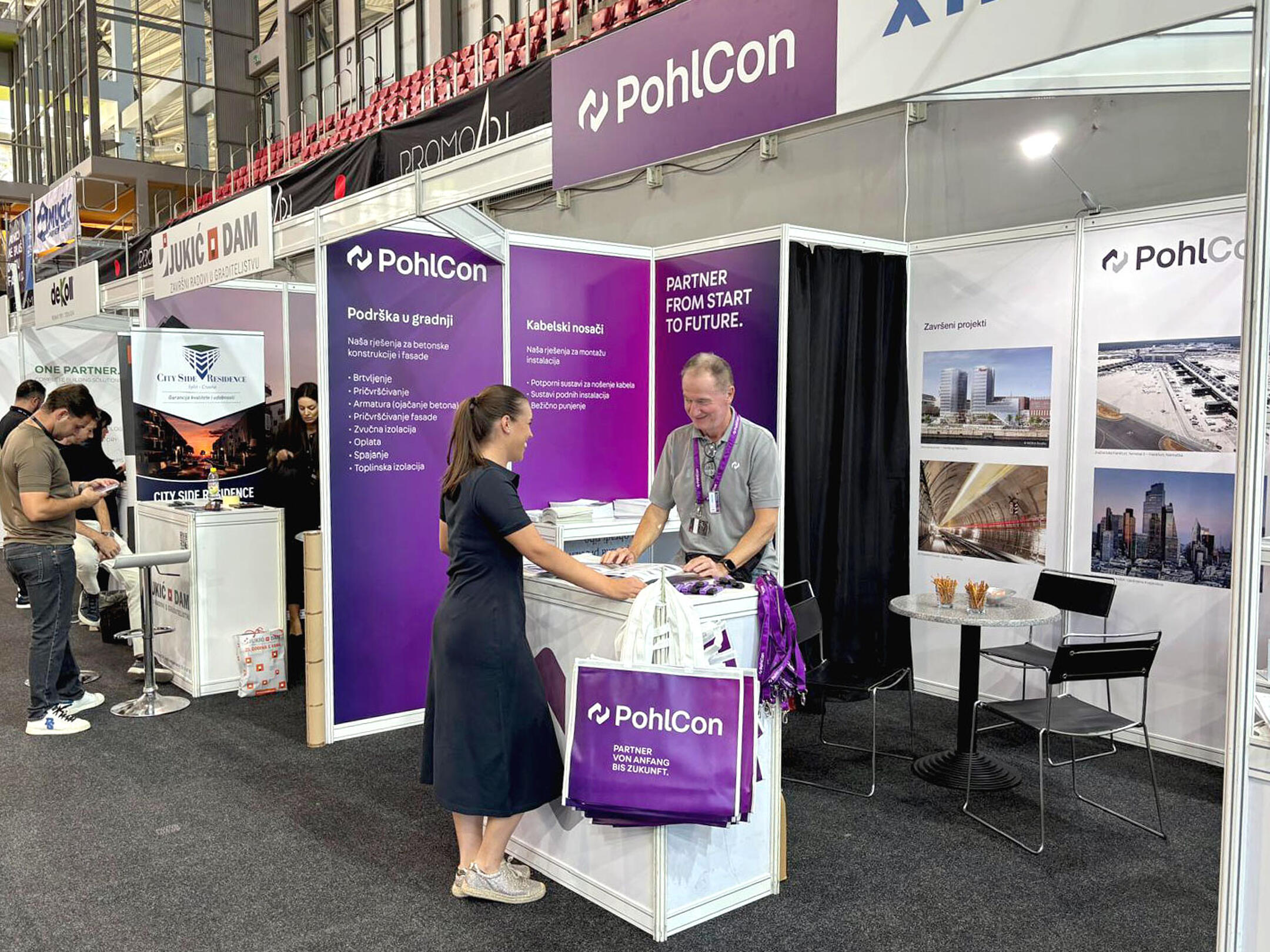 Besucherin im Gespräch mit einem PohlCon-Mitarbeiter am Messestand mit Produktinformationen und Referenzprojekten.