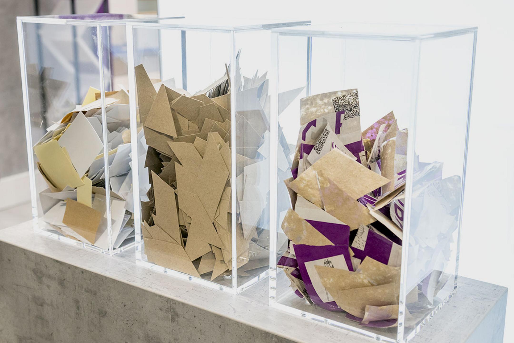 In 3 transparenten Kunststoffbehältern auf einer Betonfläche befindet sich das pappartige Schalrohr-Material.