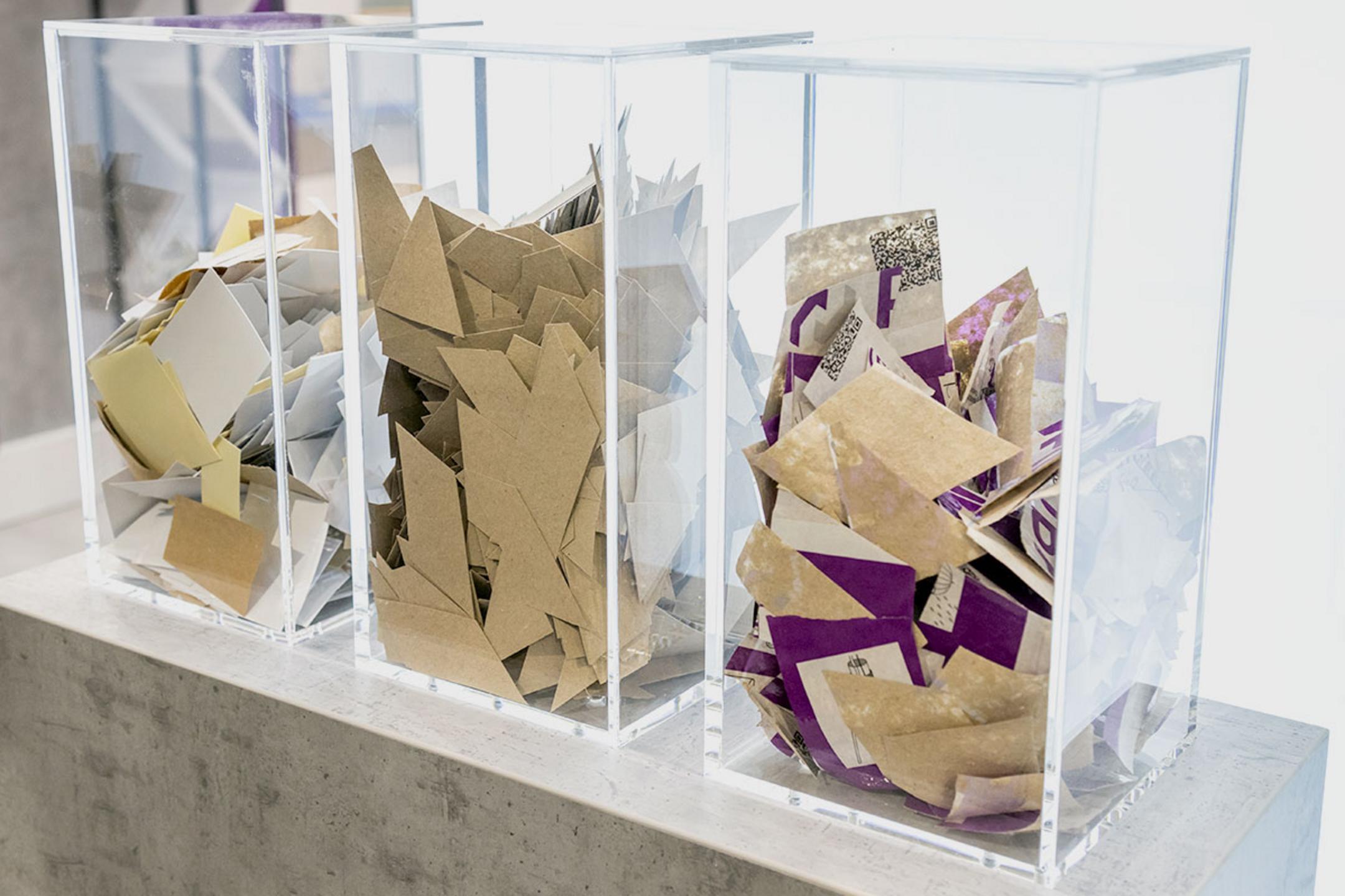 In 3 transparenten Kunststoffbehältern auf einer Betonfläche befindet sich das pappartige Schalrohr-Material.