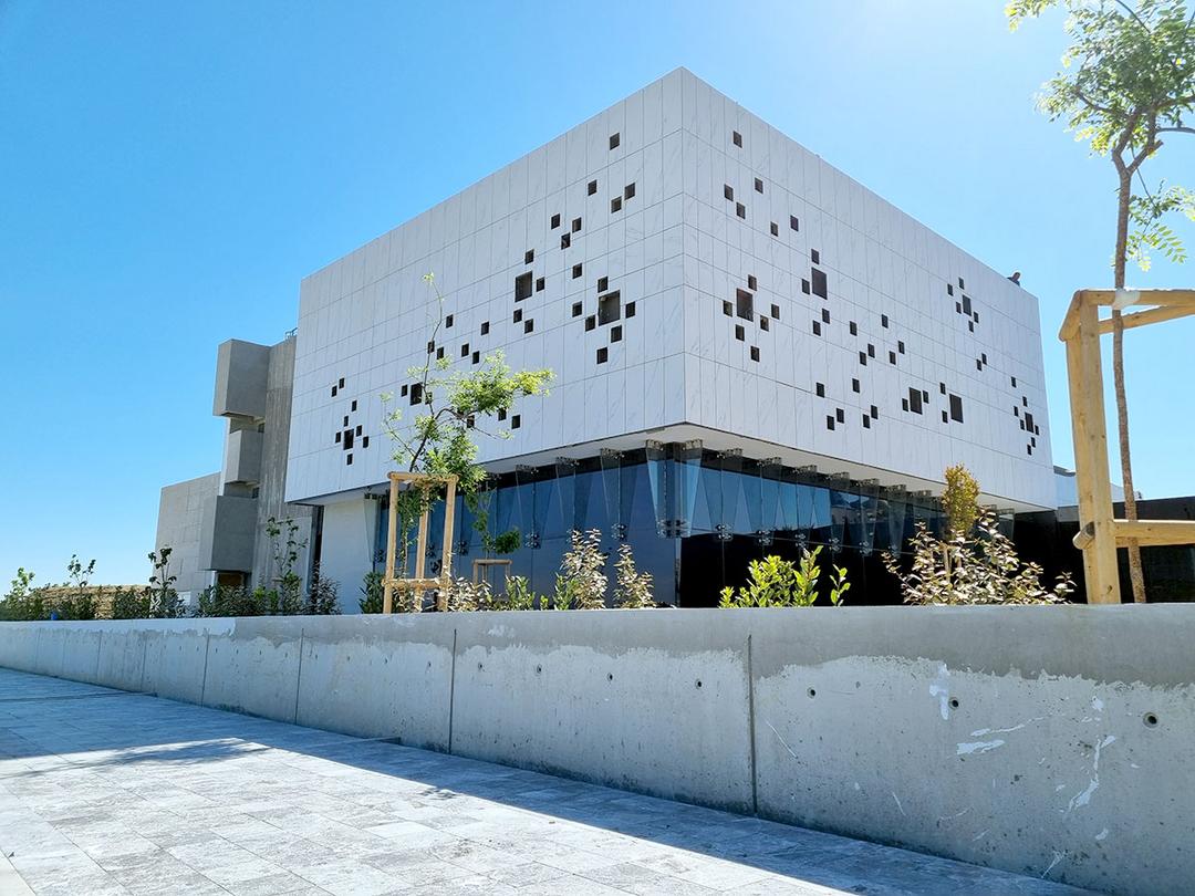 Modernes weißes Gebäude mit quadratischen Fenstern, umgeben von Pflanzen, bei strahlend blauem Himmel