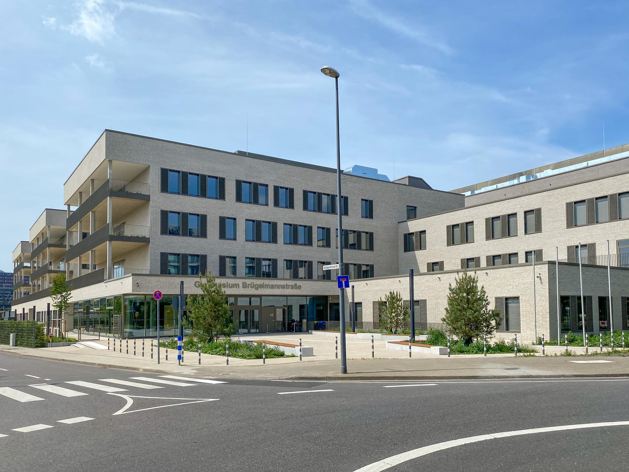 Gebäudeansicht von vorne, Bäume, blauer Himmel, Straße im Anschnitt im Vordergrund