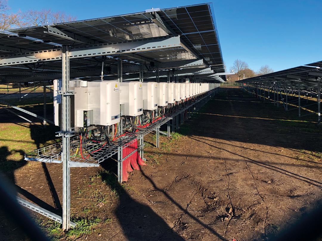 Mehrere Wechselrichter sind unter einer Solaranlage montiert und über Kabeltrassen miteinander verbunden.