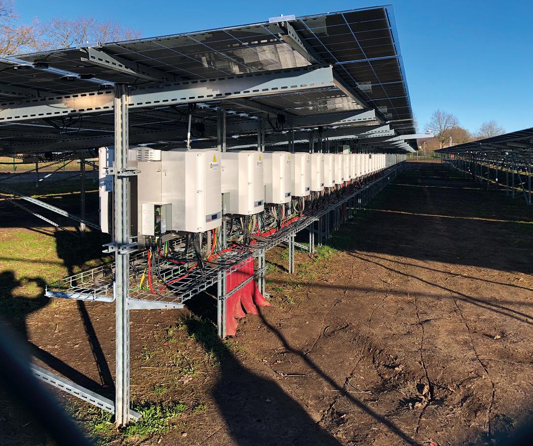 Mehrere Wechselrichter sind unter einer Solaranlage montiert und über Kabeltrassen miteinander verbunden.