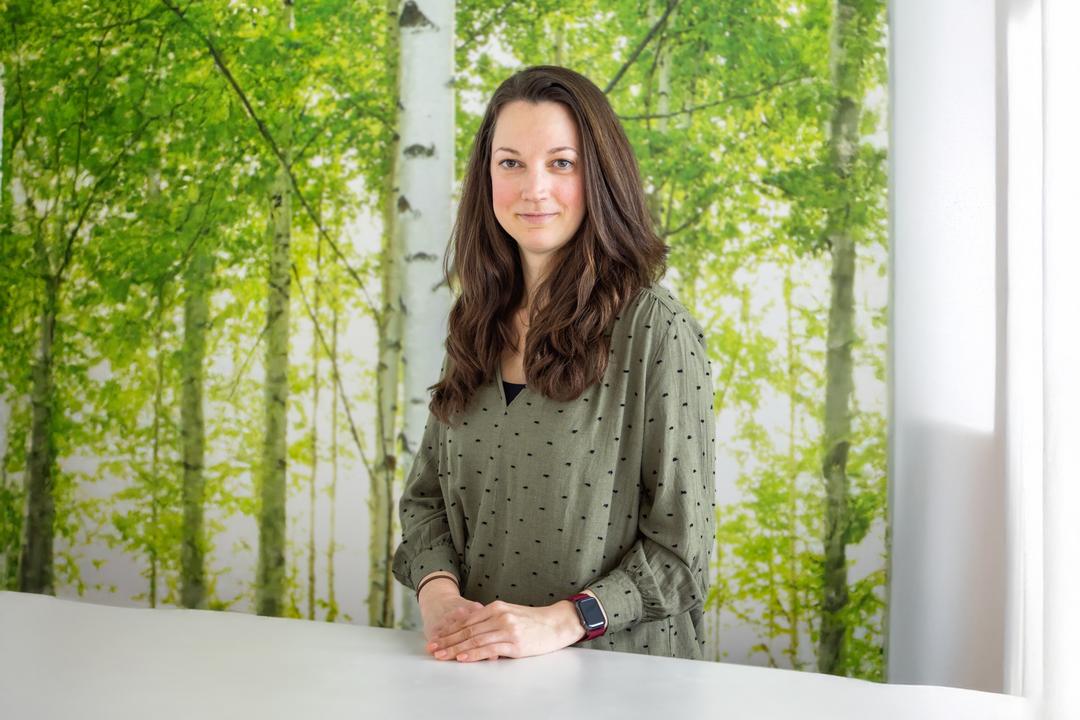 Porträtfoto einer jungen Frau mit braunem Haar vor einer Waldkulisse.