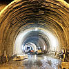 Großer, beleuchteter Tunnel im Rohbau mit Baufahrzeugen und Bauarbeiten