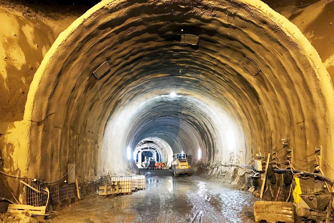 Großer, beleuchteter Tunnel im Rohbau mit Baufahrzeugen und Bauarbeiten