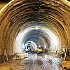Großer, beleuchteter Tunnel im Rohbau mit Baufahrzeugen und Bauarbeiten