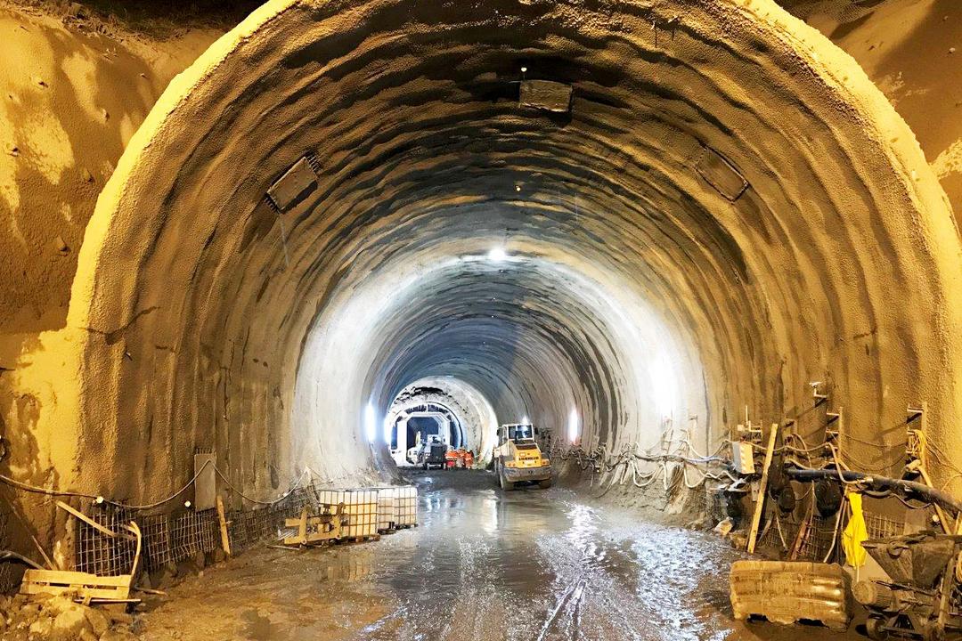 Großer, beleuchteter Tunnel im Rohbau mit Baufahrzeugen und Bauarbeiten