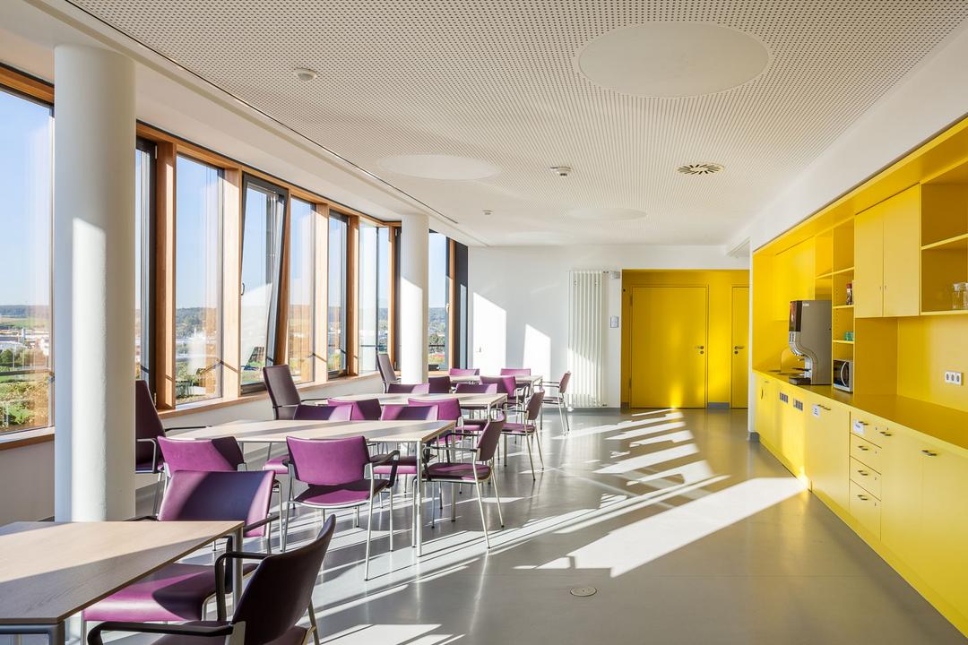 Ein lichtdurchfluteter Flur im Inneren der Klinik, mit violetten Sitzgelegenheiten und einer gelben Wand.