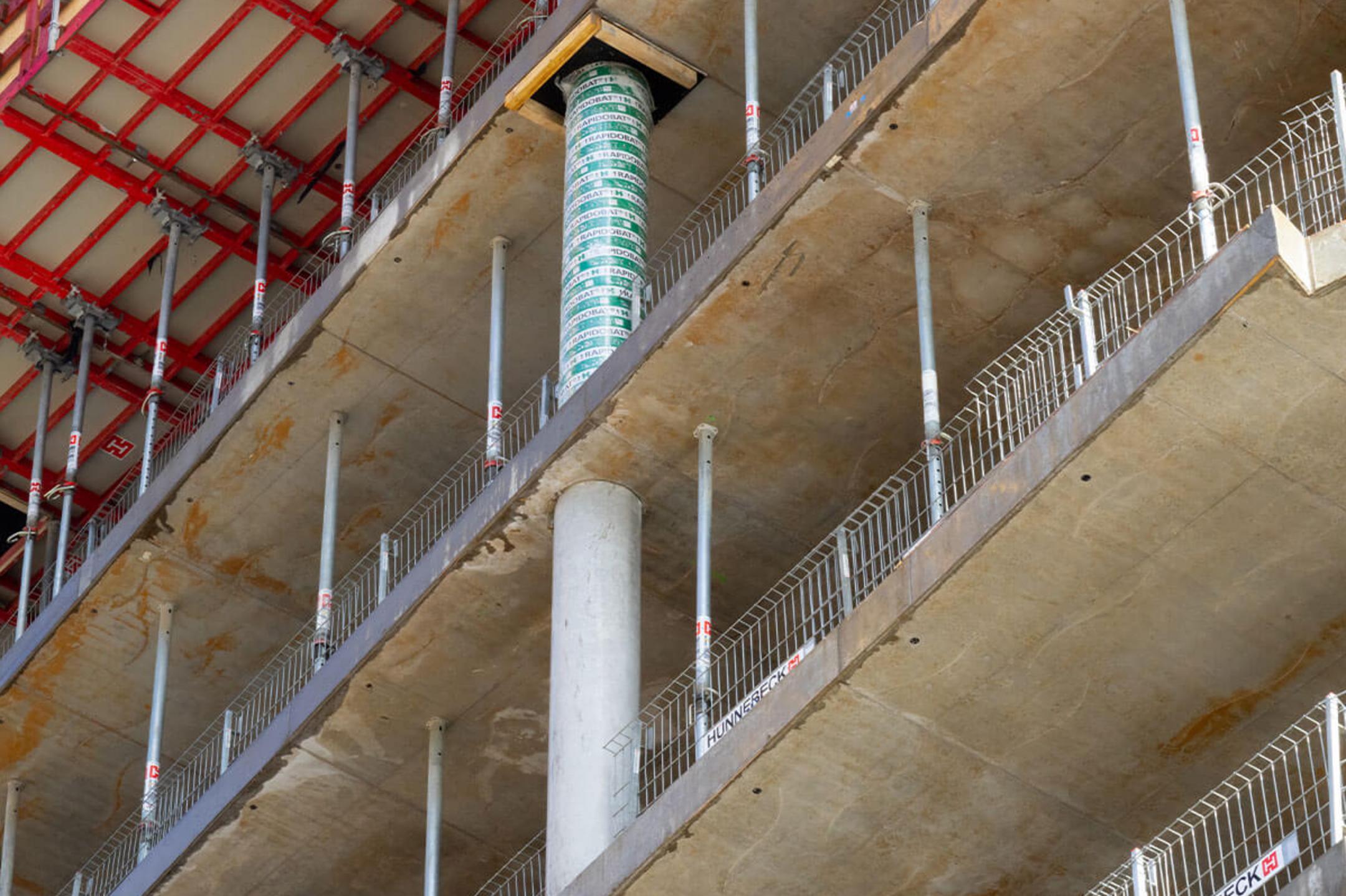 Nahaufnahme eines Baugerüsts und Schalung auf einer Baustelle, mit sichtbarem Betonpfeiler und Stützen für das nächste Stockwerk.
