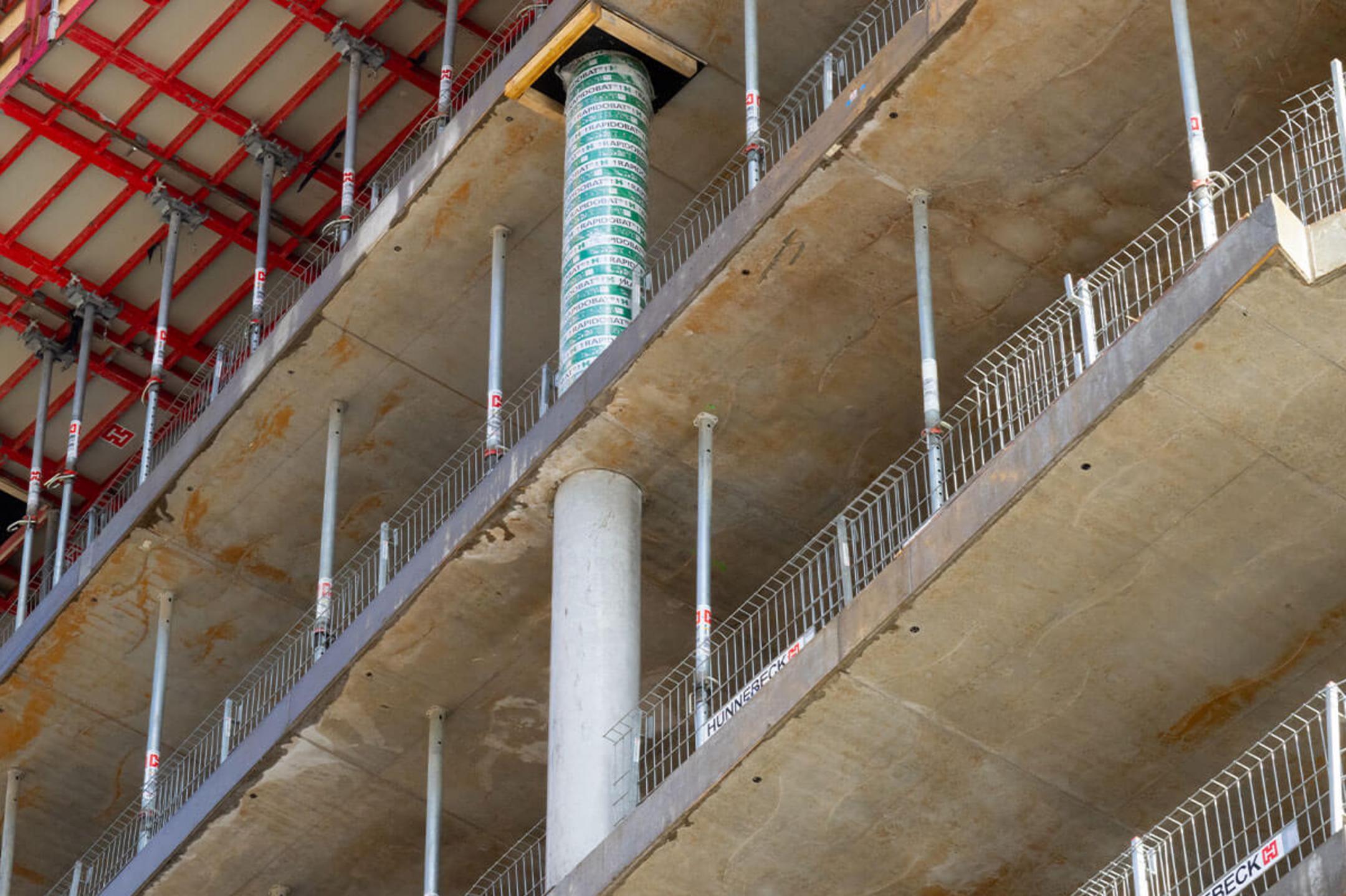Nahaufnahme eines Baugerüsts und Schalung auf einer Baustelle, mit sichtbarem Betonpfeiler und Stützen für das nächste Stockwerk.