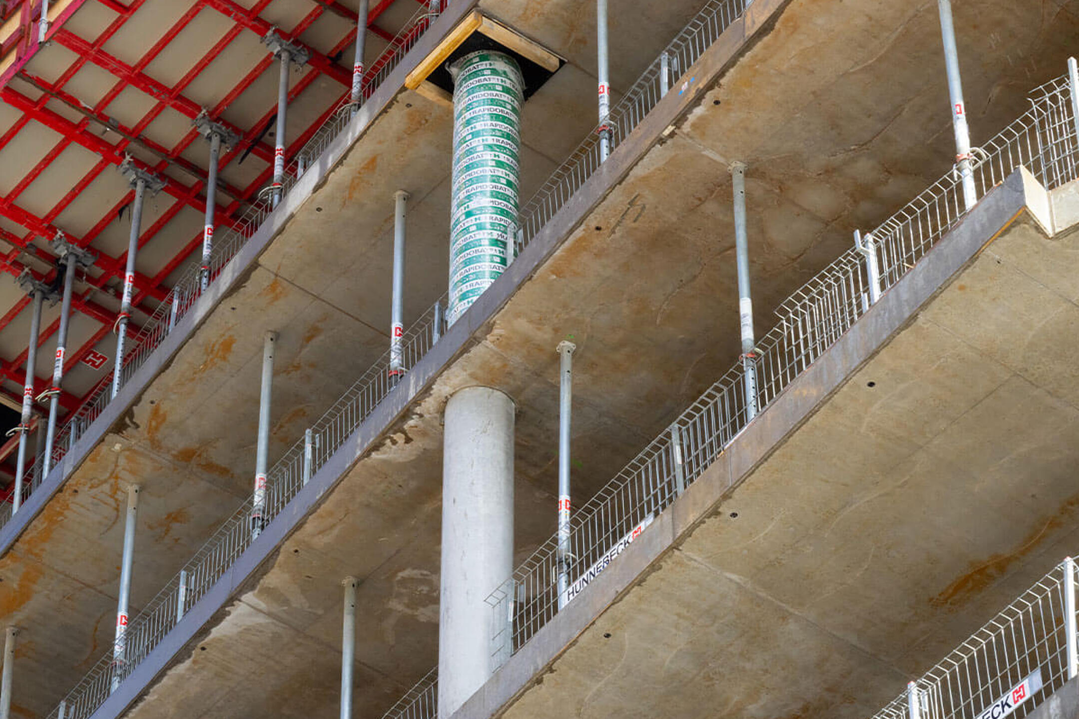 Nahaufnahme eines Baugerüsts und Schalung auf einer Baustelle, mit sichtbarem Betonpfeiler und Stützen für das nächste Stockwerk.