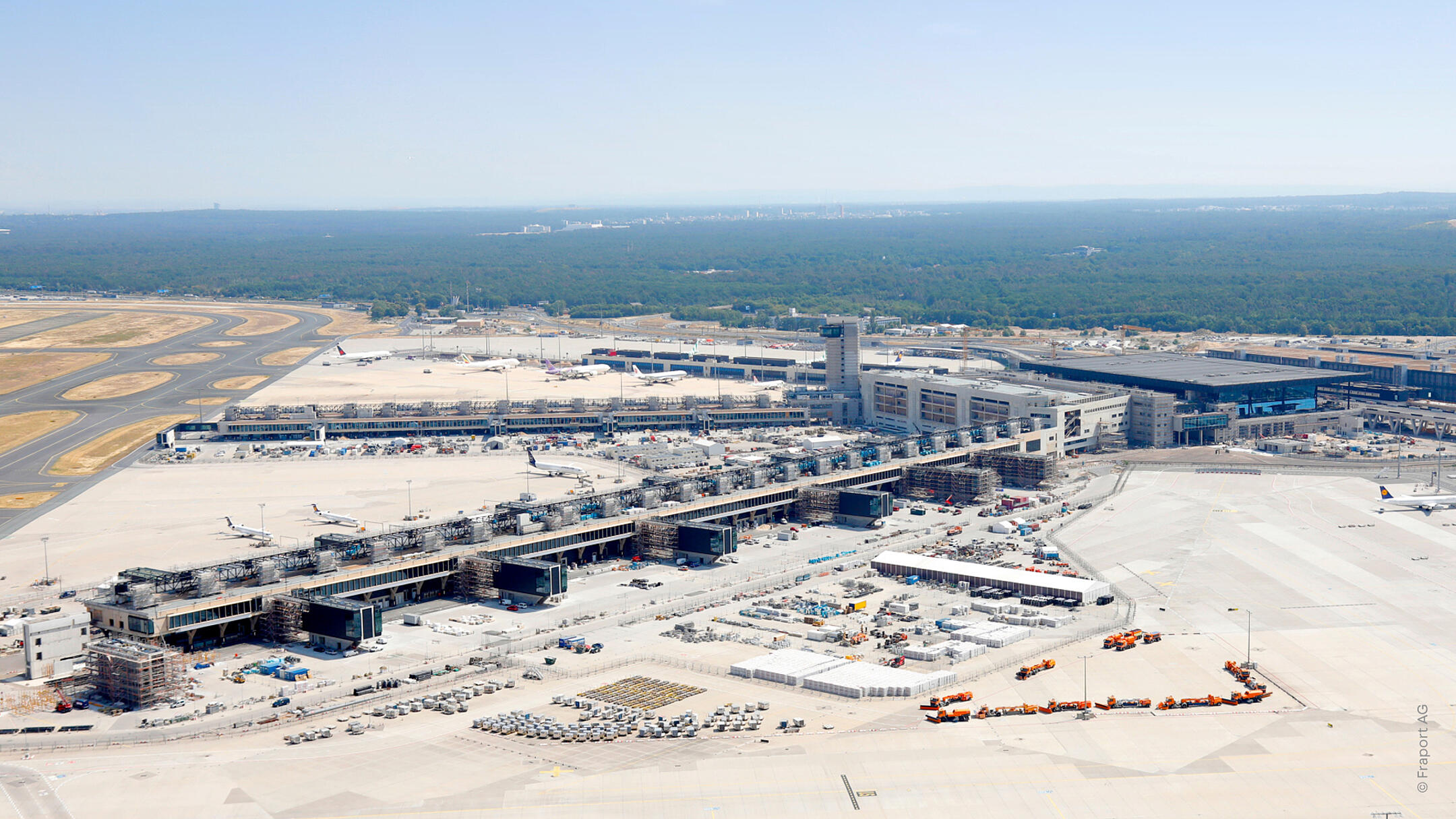 Luftaufnahme des Flughafen-Terminalbaus mit Rollfeldern, Flugzeugen, Gebäuden und umliegendem Waldgebiet