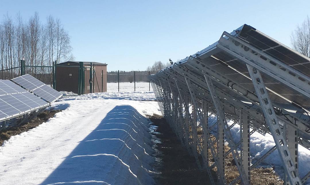 Photovoltaikanlage mit robustem Stahluntergestell im Schnee, PV-Module aufgeständert, Technikhaus und Zaun im Hintergrund.