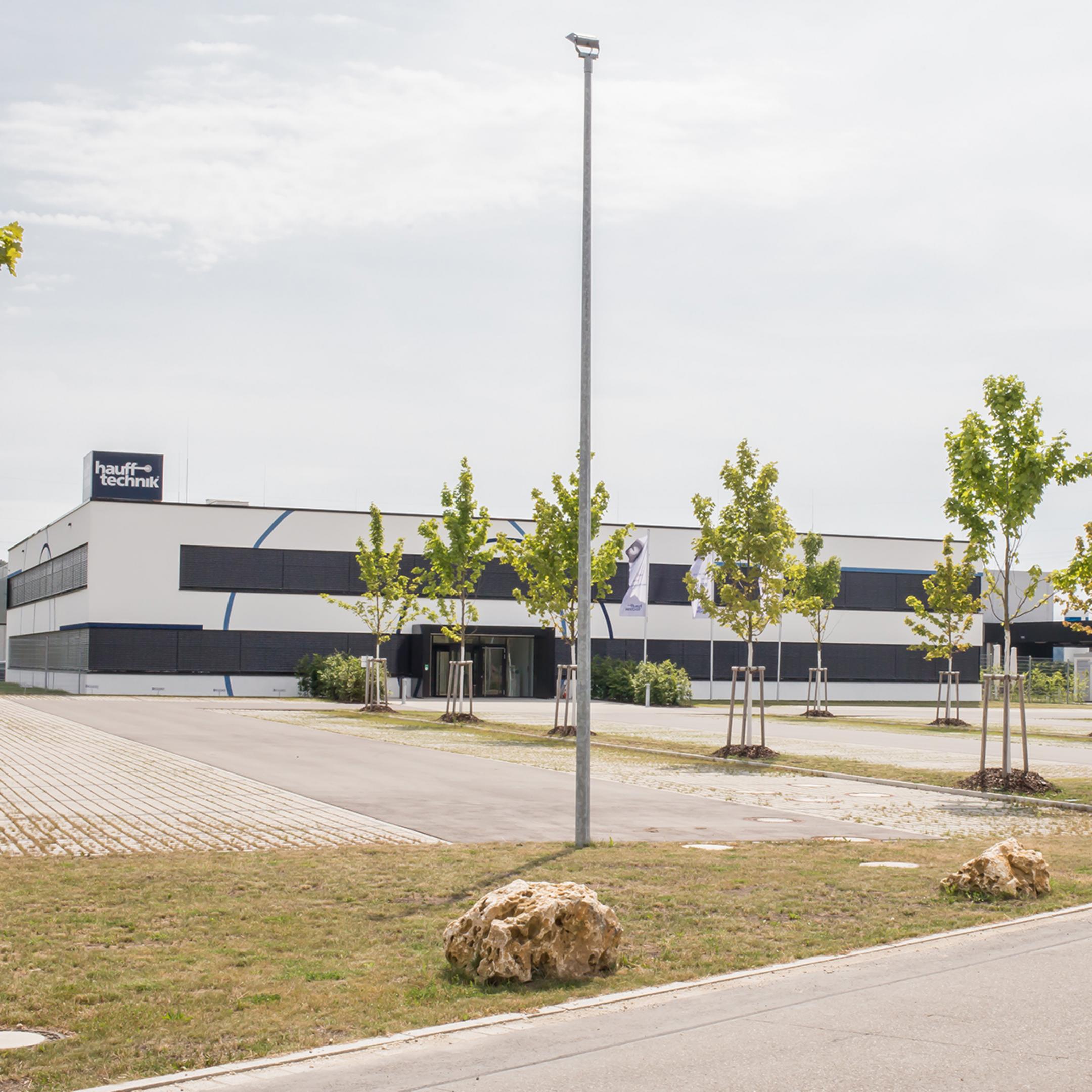 Der Firmenneubau von Weitem gesehen, im Vordergrund grün bepflanzte Parkplätze.